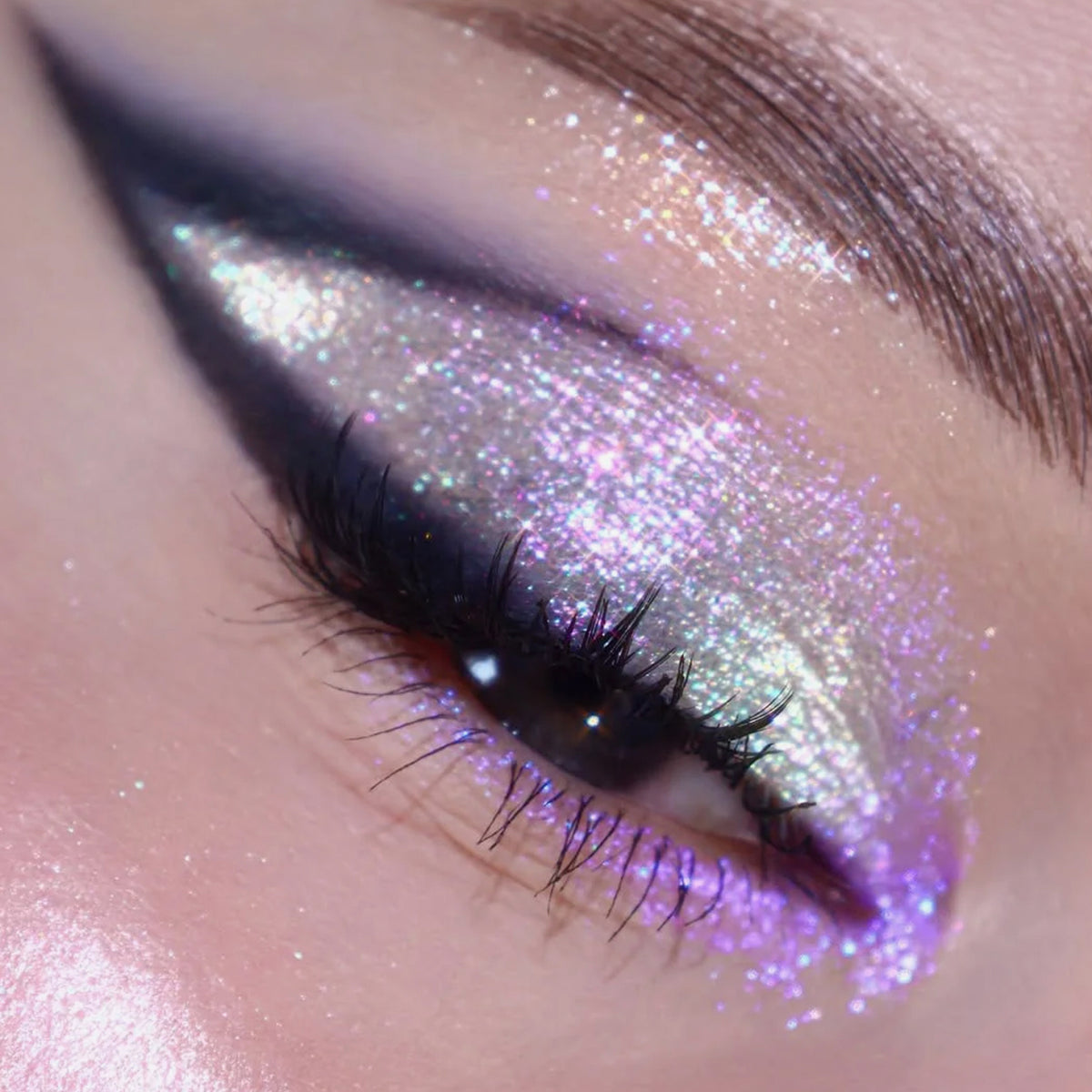 Geschlossenes Auge mit dramatischem  schwarzen Eyeliner und intensiv schimmerndem lila und silbernem Glitzer.