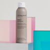 Eine Dose Living Proof No Frizz Instant De-Frizzer wird vor geometrischen Formen in Pastellrosa und Blau präsentiert.