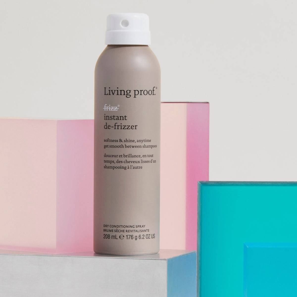 Eine Dose Living Proof No Frizz Instant De-Frizzer wird vor geometrischen Formen in Pastellrosa und Blau präsentiert.