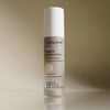 Eine Flasche Living Proof No Frizz Smooth Styling Serum ist auf einem beigen Hintergrund mit Farbverlauf abgebildet.