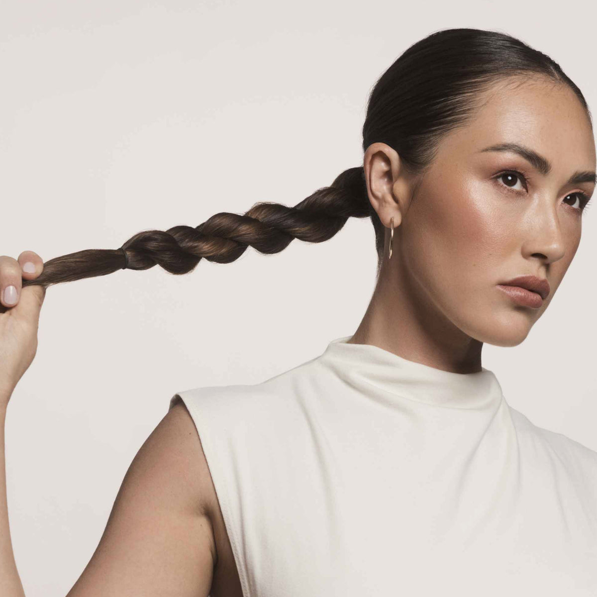 Eine Frau mit geflochtenem Zopf hält ihren Zopf zur Seite und zeigt glatte Ergebnisse mit dem Living Proof No Frizz Smooth Styling Spray.