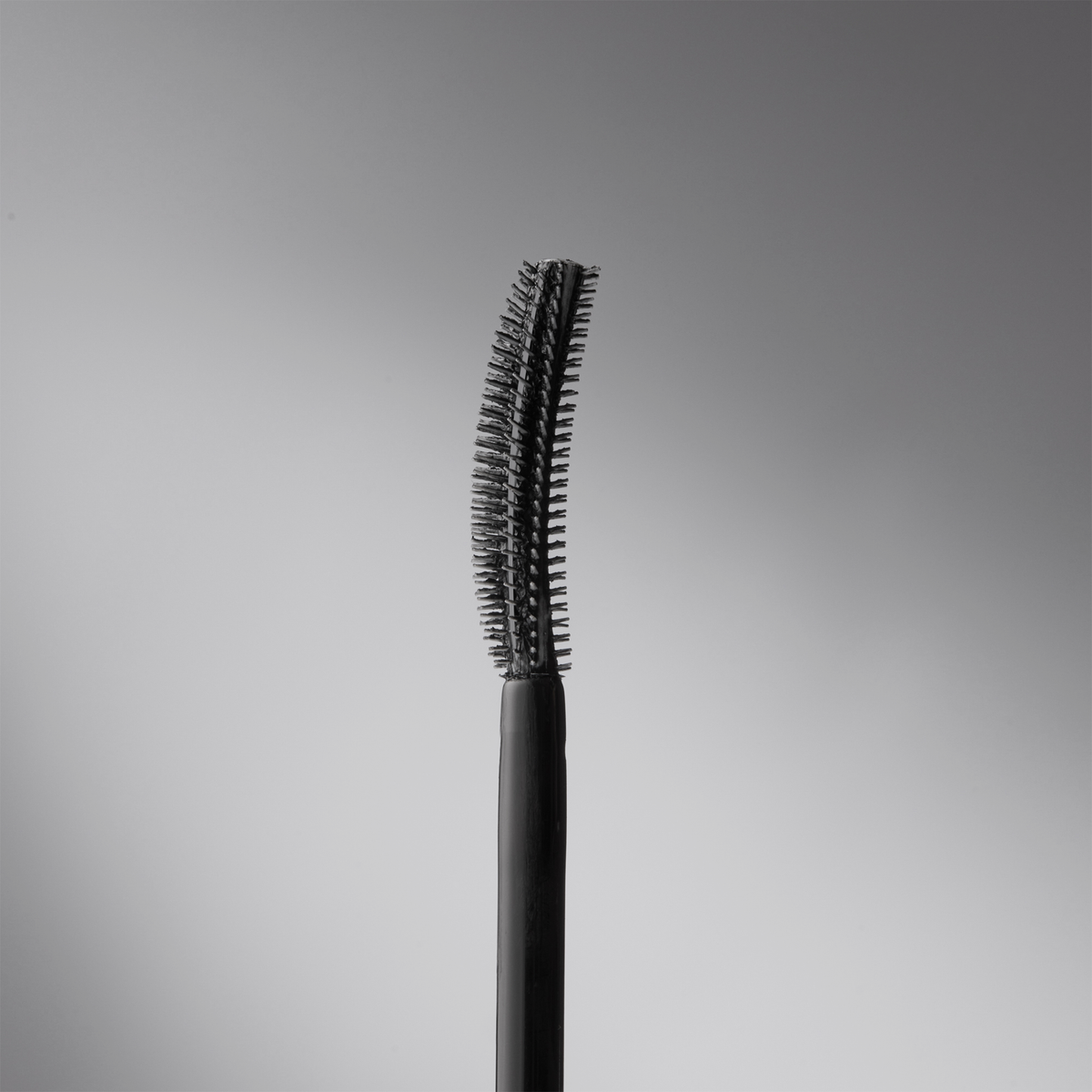 Eine Nahaufnahme des schwarzen, gebogenen Mascarastifts THE GLAM FEMULINE von Mesauda Beauty vor einem schlichten grauen Hintergrund.