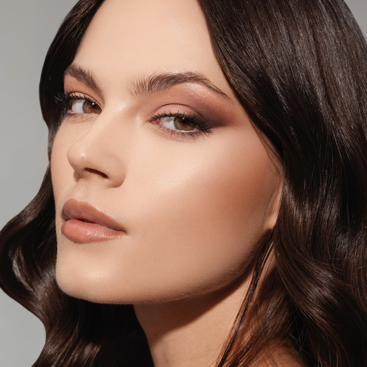 Eine Frau mit braunen Haaren und Smokey-Eye-Make-up aus der ARCHETYPE II Palette blickt vor neutralem Hintergrund in die Kamera.