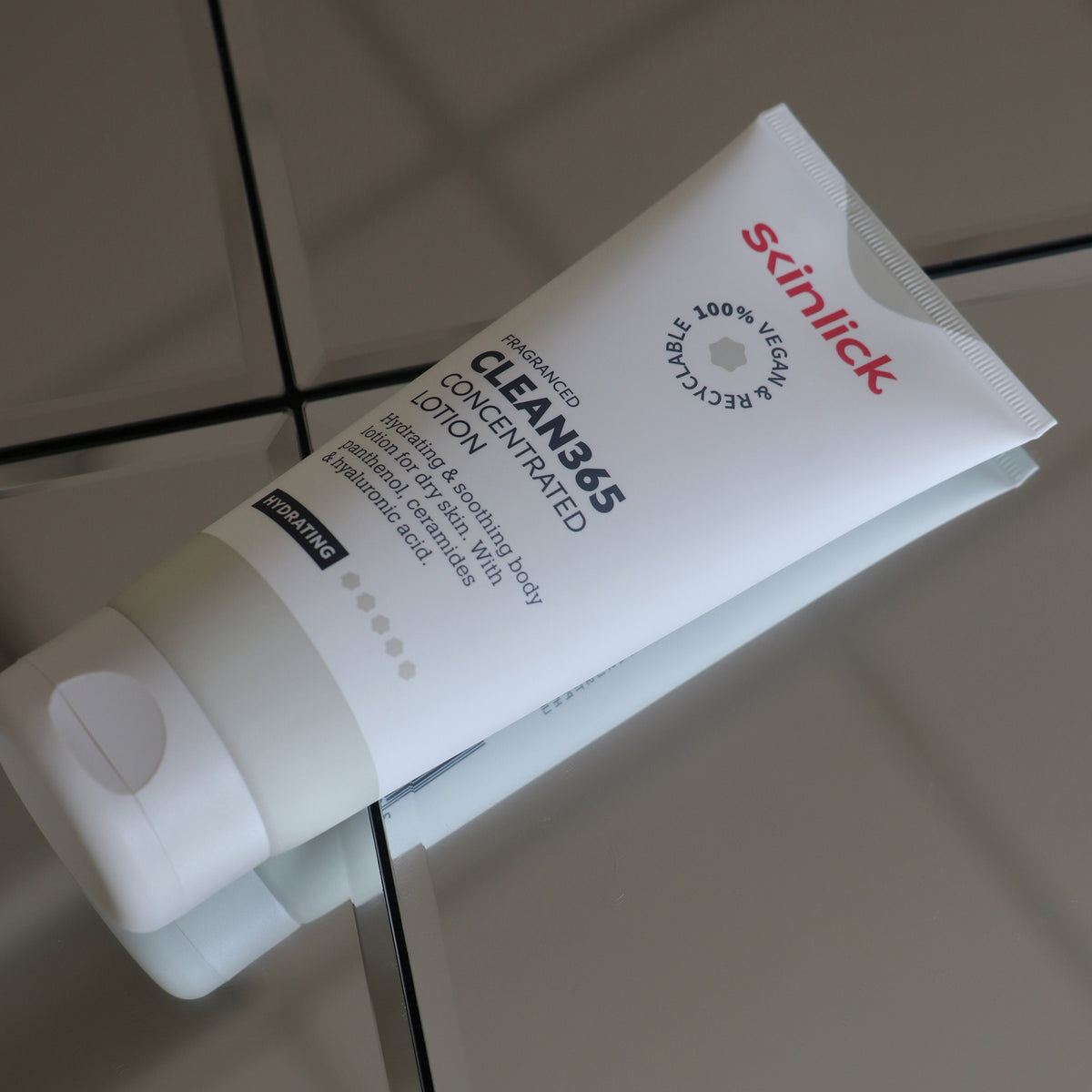 Eine weiße Tube Clean365 Concentrated Lotion liegt auf einer reflektierenden gefliesten Oberfläche.
