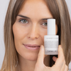 Eine Frau hält eine Flasche Ceramide Repair Moisturizer vor ihr Gesicht und blickt in die Kamera.