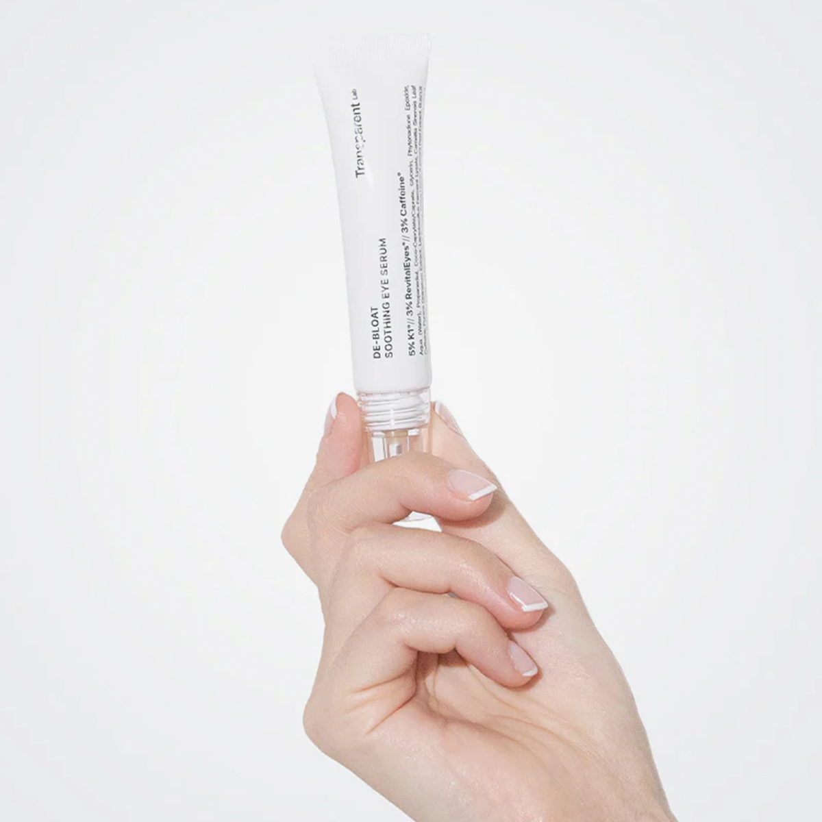 Hand hält eine kleine Tube De-Bloat Soothing Eye Serum vor einem schlichten Hintergrund.