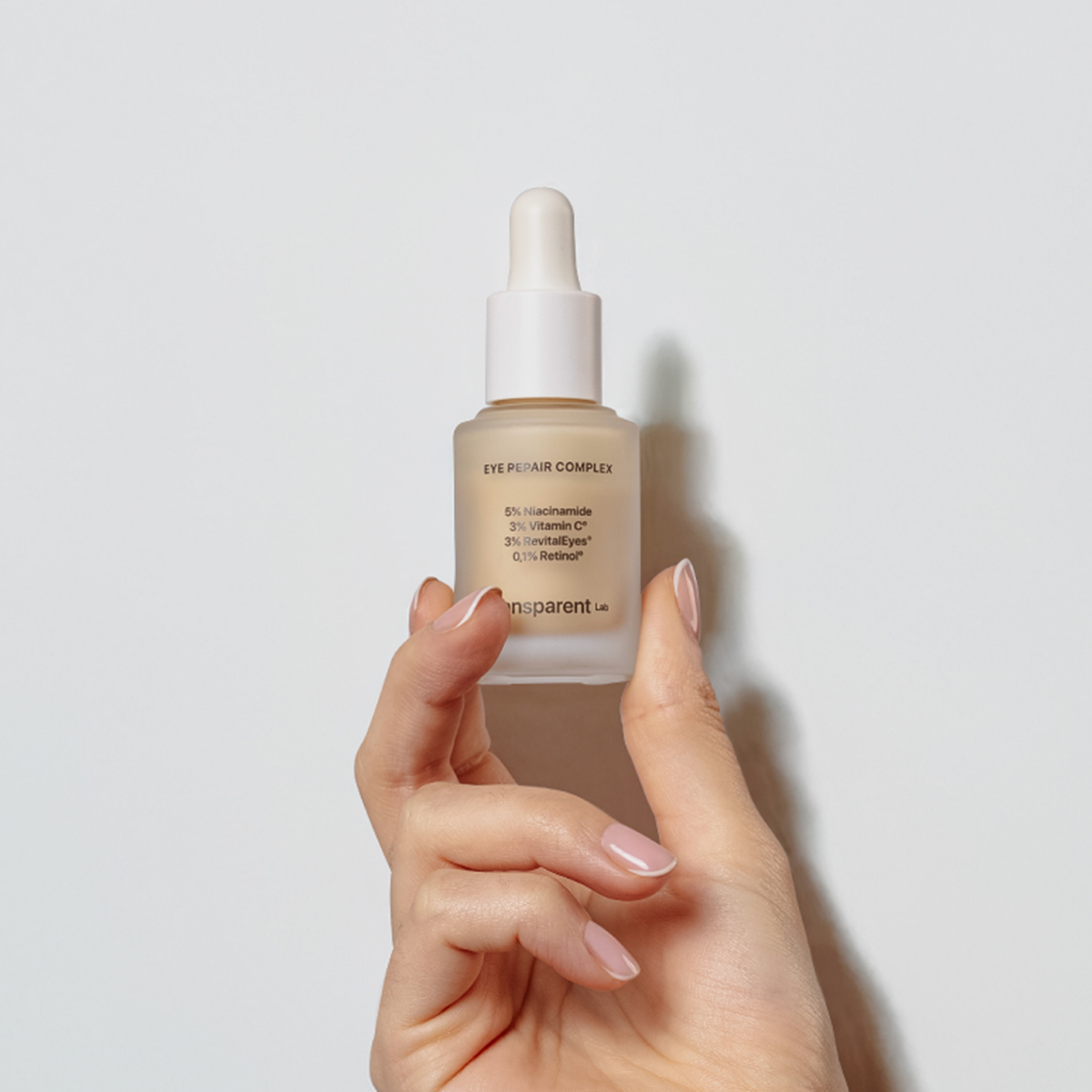 Eine Hand hält eine Tropfflasche mit Eye Repair Complex vor einem weißen Hintergrund.