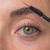 Eine Nahaufnahme des Auges einer Person, bei der die Wimpernwachstums-Mascarabürste die Augenbraue pflegt.