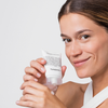 Lächelnde Frau, die die Flasche Niacinamide Glow Cream mit dem Produkt auf den Fingern vor einem weißen Hintergrund hält.