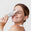 Lächelnde Frau, die eine Flasche Pure Glycerin Face Serum vor ihr Gesicht hält, die Augen geschlossen hat und einen natürlichen Blick ausstrahlt.