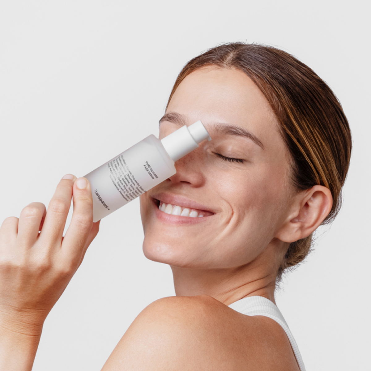 Lächelnde Frau, die eine Flasche Pure Glycerin Face Serum vor ihr Gesicht hält, die Augen geschlossen hat und einen natürlichen Blick ausstrahlt.