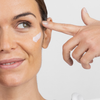 Eine Frau trägt sanft Retinal Age Reverse Cream unter ihrem Auge auf und lächelt leicht.