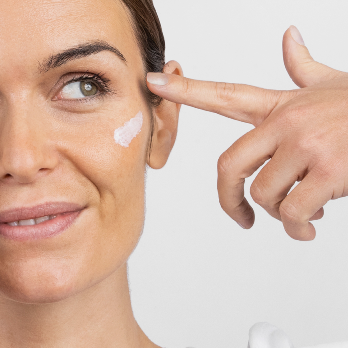 Eine Frau trägt sanft Retinal Age Reverse Cream unter ihrem Auge auf und lächelt leicht.