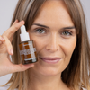 Frau lächelt in die Kamera, während sie eine Flasche Super C Serum an ihre rechte Wange hält.