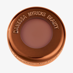 Runder bronzener Tiegel des Danessa Myricks Mini Yummy Skin Blurring Balm Powder Flushed - Spiced Latte mit Fenster zum Rostrotem Inhalt.
