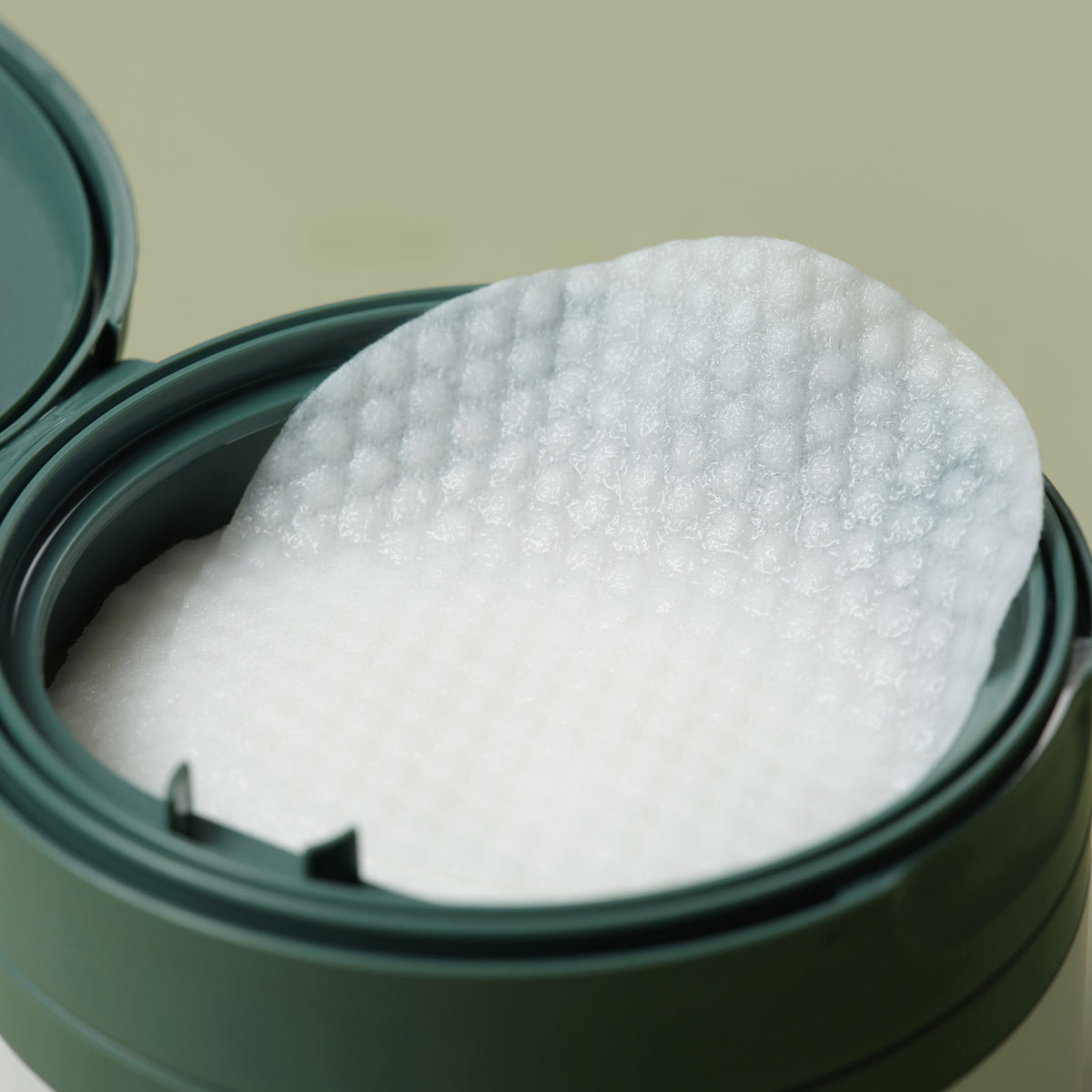 Eine Nahaufnahme des Heartleaf 77 % Toner Pads, das sein strukturiertes Wattepad in einem grünen Plastikbehälter mit geöffnetem Deckel zeigt.