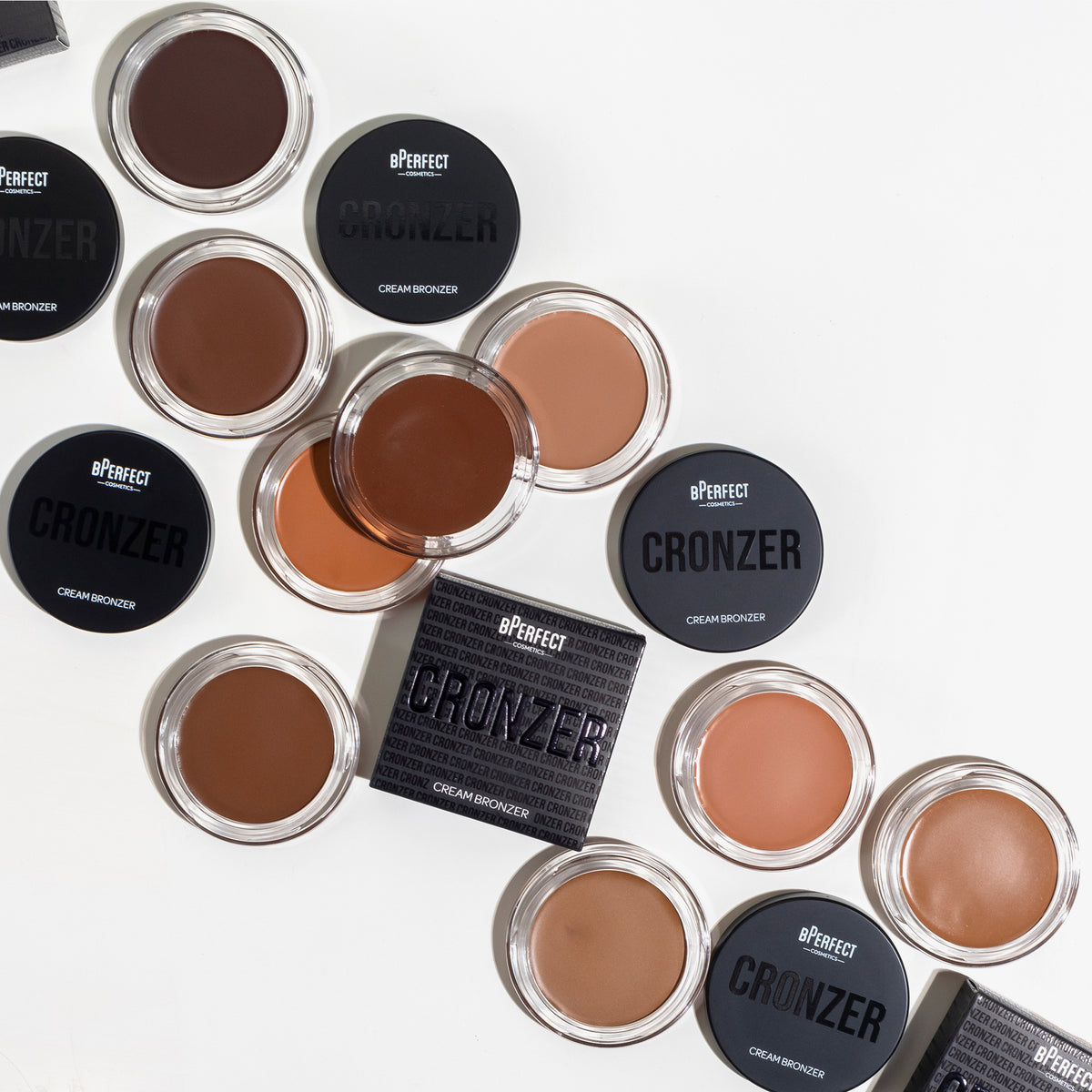 Mehrere geöffnete und geschlossene Tiegel des bPerfect Cronzer Cream Bronzers in verschiedenen Brauntönen auf weißem Hintergrund.