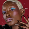 Eine Frau mit dunklem Teint und blondiertem kurzen Haar trägt auffälliges Make-up aus der Love is Love-Palette.