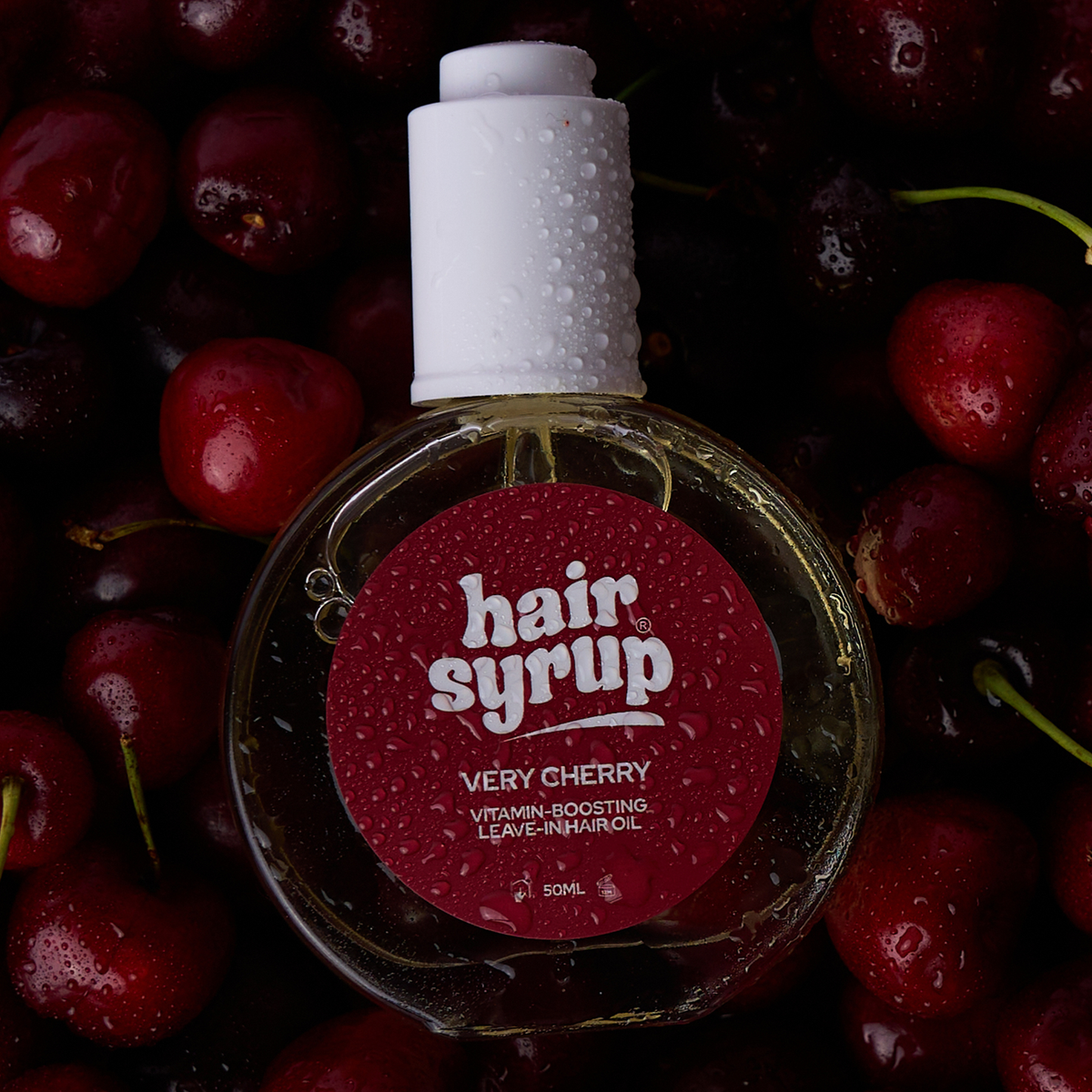 Eine Flasche Very Cherry von Hair Syrup mit Wassertropfen liegt auf dunklen Kirschen.
