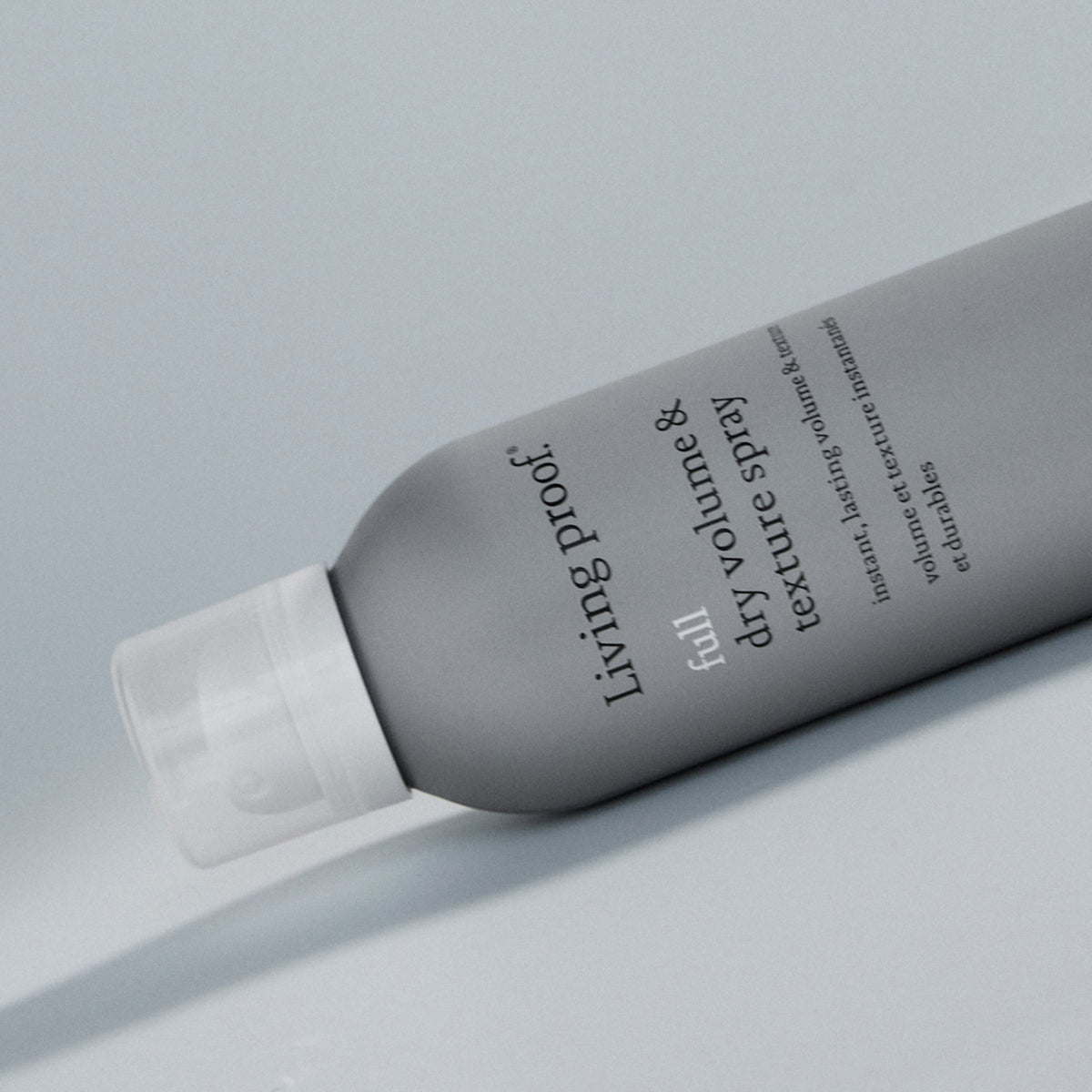 Eine Flasche Living Proof Full Dry Volume & Texture Spray in Grau steht auf einer hellen Oberfläche.