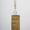 Vor einem schlichten Hintergrund gibt eine Pipette Öl in eine Flasche „Living Proof No Frizz Vanishing Oil“ ab.