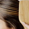 Eine Person bürstet ihr hellbraunes und blondes Haar mit einer Holzhaarbürste und verwendet dabei den Perfect Hair Day Healthy Hair Perfector von Living Proof.