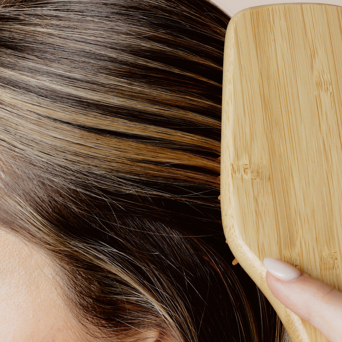 Eine Person bürstet ihr hellbraunes und blondes Haar mit einer Holzhaarbürste und verwendet dabei den Perfect Hair Day Healthy Hair Perfector von Living Proof.
