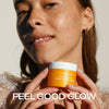 Eine Frau lächelt und hält einen Tiegel Lumene NORDIC C [VALO] Tagescreme SPF 30. Der Text lautet: FEEL GOOD GLOW.