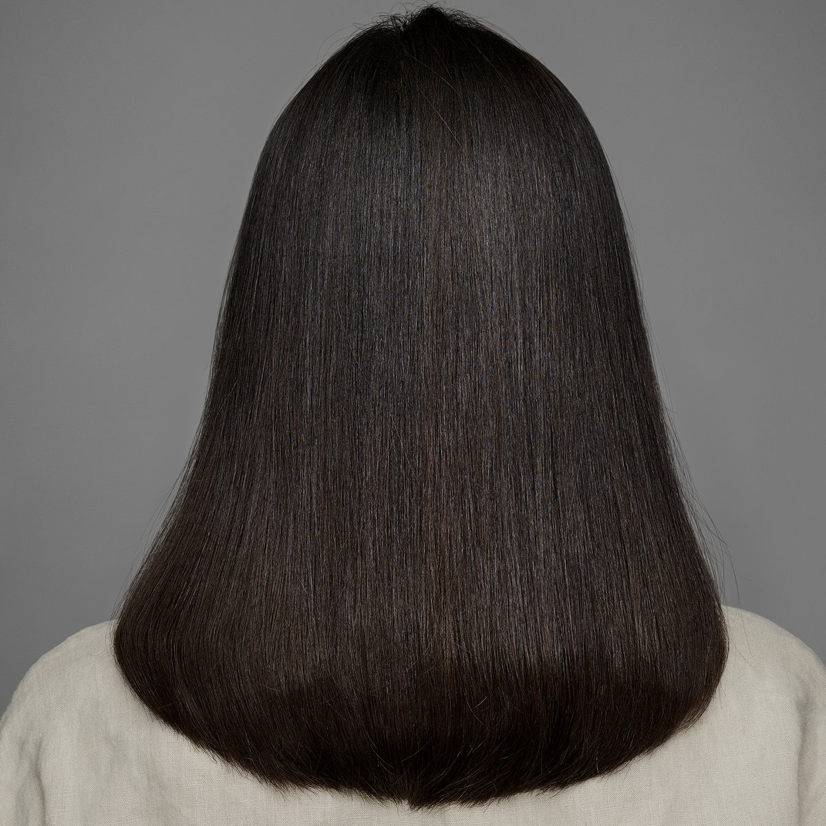 Eine Person mit glattem, glänzendem, dunkelbraunem Haar, von hinten, zeigt das Ergebnis der Anwendung von maria nila's True Soft Shampoo.