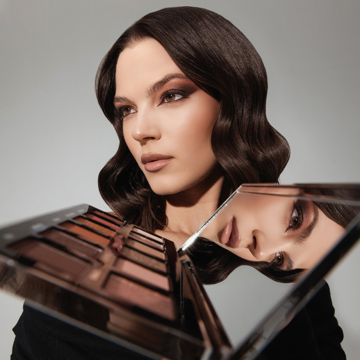 Eine Frau mit welligem Haar und dramatischem Augen-Make-up; vor ihr die geöffnete ARCHETYPE II Palette mit Spiegel.