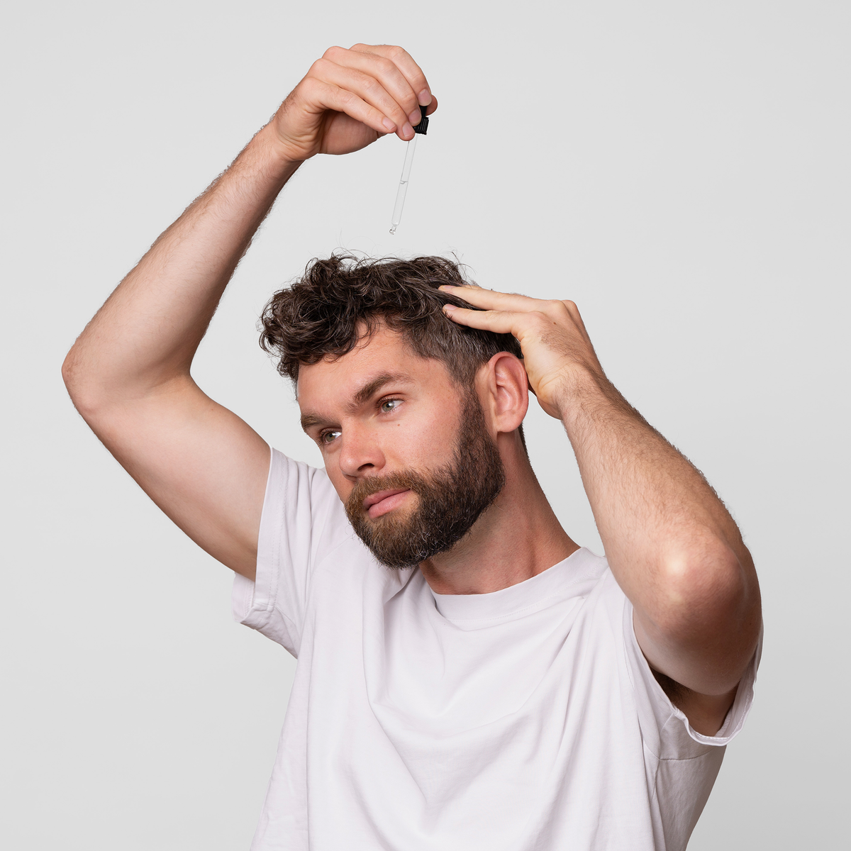 Ein Mann mit weißem T-Shirt trägt Scandinavian Biolabs Bio Plixin Serum+ Men mit einer Pipette auf seine Kopfhaut auf.