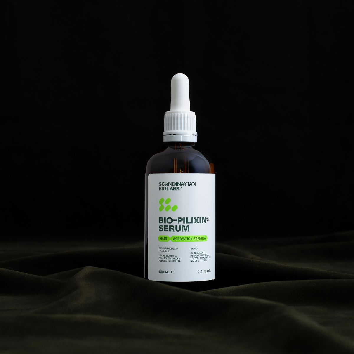 Eine braune Tropfflasche mit der Aufschrift "Bio-Pilixin® Serum+" von Scandinavian Biolabs steht auf einem dunklen, drapierten Stoffhintergrund.