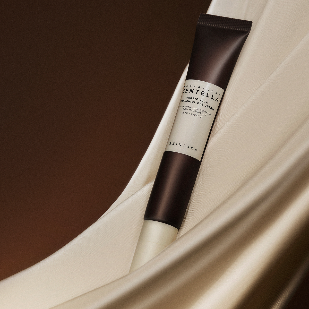 Auf weichen, beigen Stofffalten liegt eine Tube SKIN1004 Madagascar Centella Probio-Cica Bakuchiol Eye Cream.
