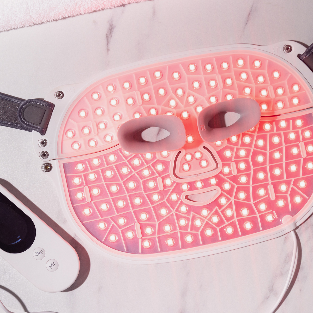 Die STYLPRO Wavelength Pro 5 in 1 LED-Maske mit roten Lichtern wird flach auf einer Marmorfläche neben der Fernbedienung präsentiert.