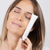 Eine Frau mit hellbraunem Haar hält eine Tube P.I.E. Acne Red Spot Fading Treatment vor ihr Gesicht, hat die Augen geschlossen und lächelt sanft.