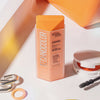 Eine Flasche Technocolor Self Tanning Face Serum Caramel auf einer weißen Fläche, umgeben von Make-up-Artikeln.