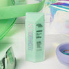 Technocolor Self Tanning Face Serum Emerald in einer grünen Flasche vor einem lebendigen Hintergrund mit Accessoires.