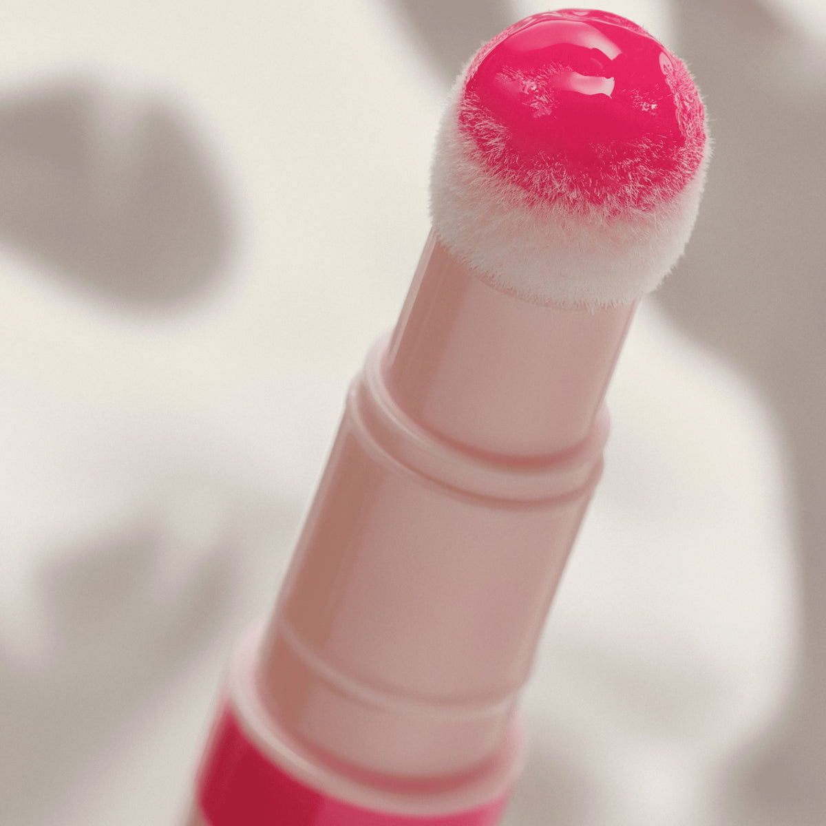 Nahaufnahme eines Applikators mit glänzendem pinkem Lip Oil, die Spitze ist flauschig und mit Farbe benetzt.
