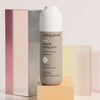 Eine Flasche Living Proof No Frizz Smooth Styling Spray steht auf einem pastellfarbenen geometrischen Hintergrund.