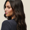 Eine Frau mit langem, welligem, dunklem Haar, gestylt mit Living Proof No Frizz Vanishing Oil, vor einem hellen Hintergrund.