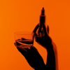 Hände halten ein Glas Wasser und eine Bio-Silacumin-Tropfflasche von Scandinavian Biolabs vor einem orangefarbenen Hintergrund.