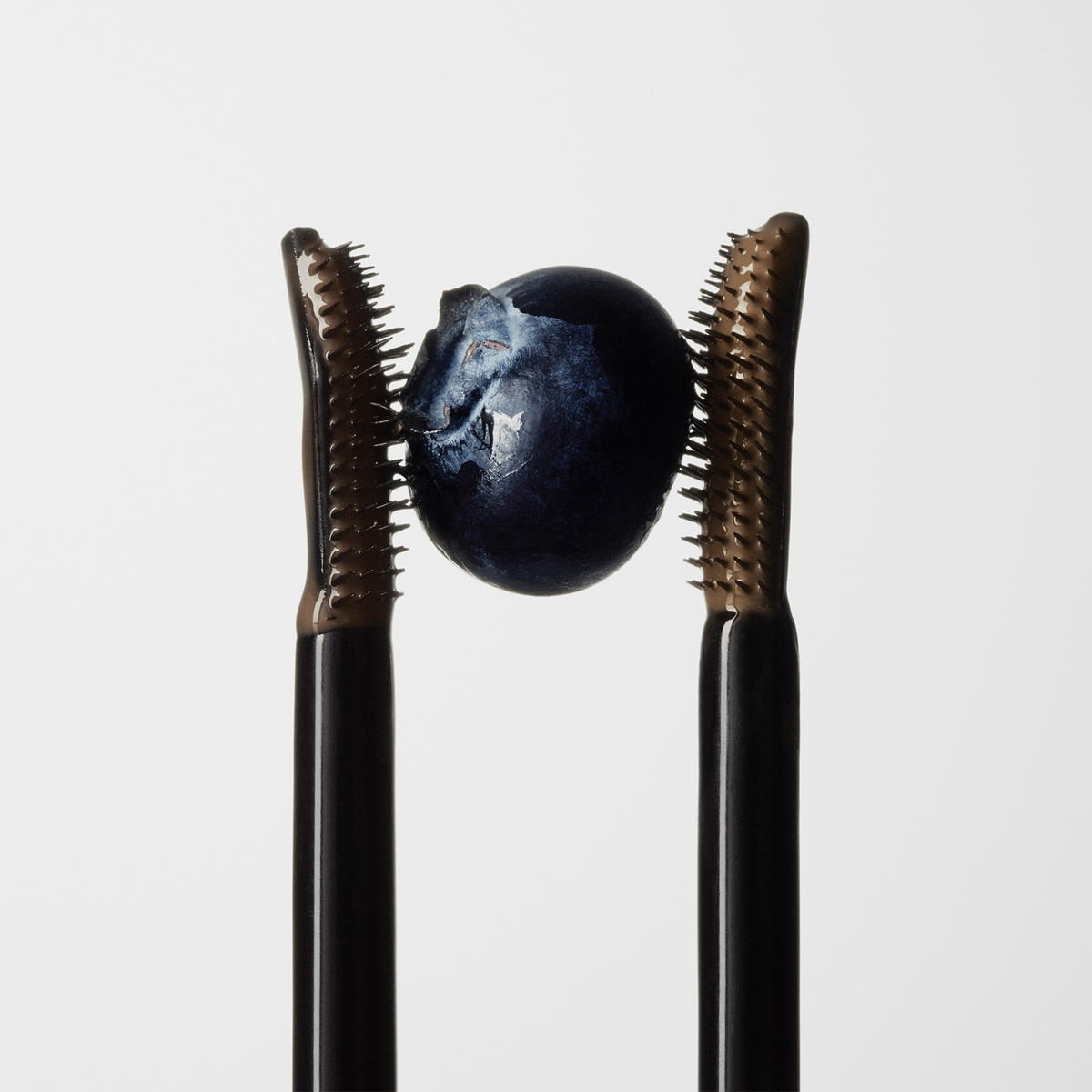 Zwei XLASH Brow Booster-Applikatoren, zwischen deren Bürsten jeweils eine Heidelbeere liegt.
