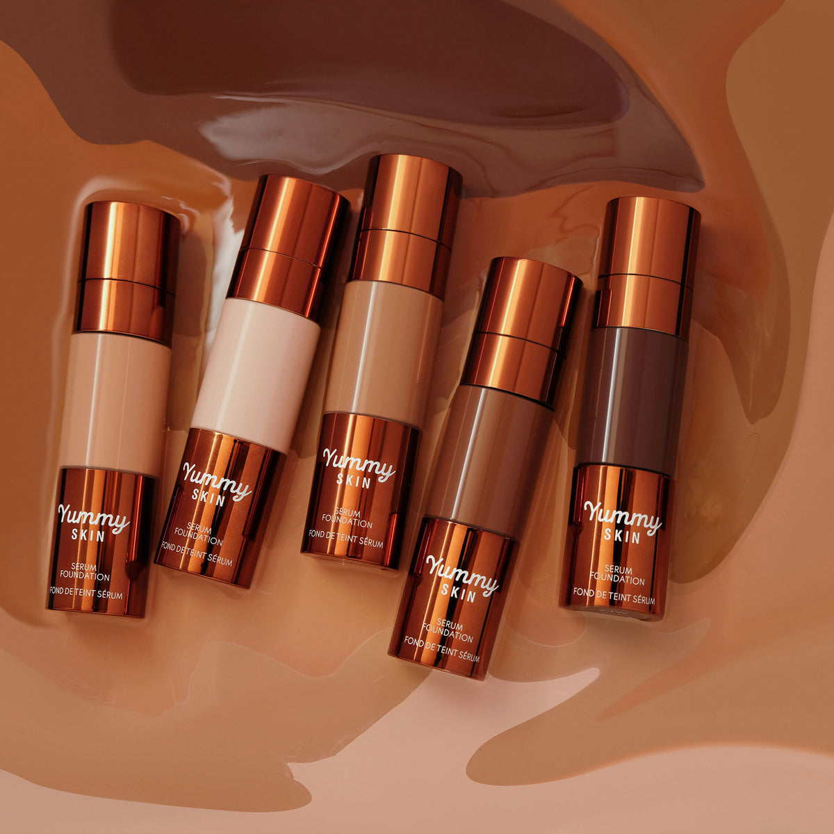 Fünf Yummy Skin Serum Foundations in unterschiedlichen Farben liegen in flüssiger Foundation.