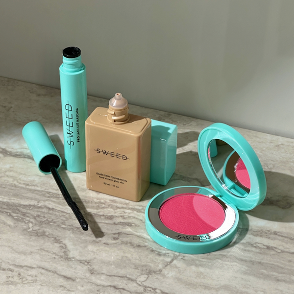Drei Make-up-Produkte von SWEEED: Mascara, flüssige Foundation und ein rosa Rouge-Kompakt mit Spiegel auf einer Marmoroberfläche.