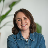 Porträt von Leanne mit braunen Haaren, blaunen Augen und blauer Jeansjacke vor hellem Hintergrund.