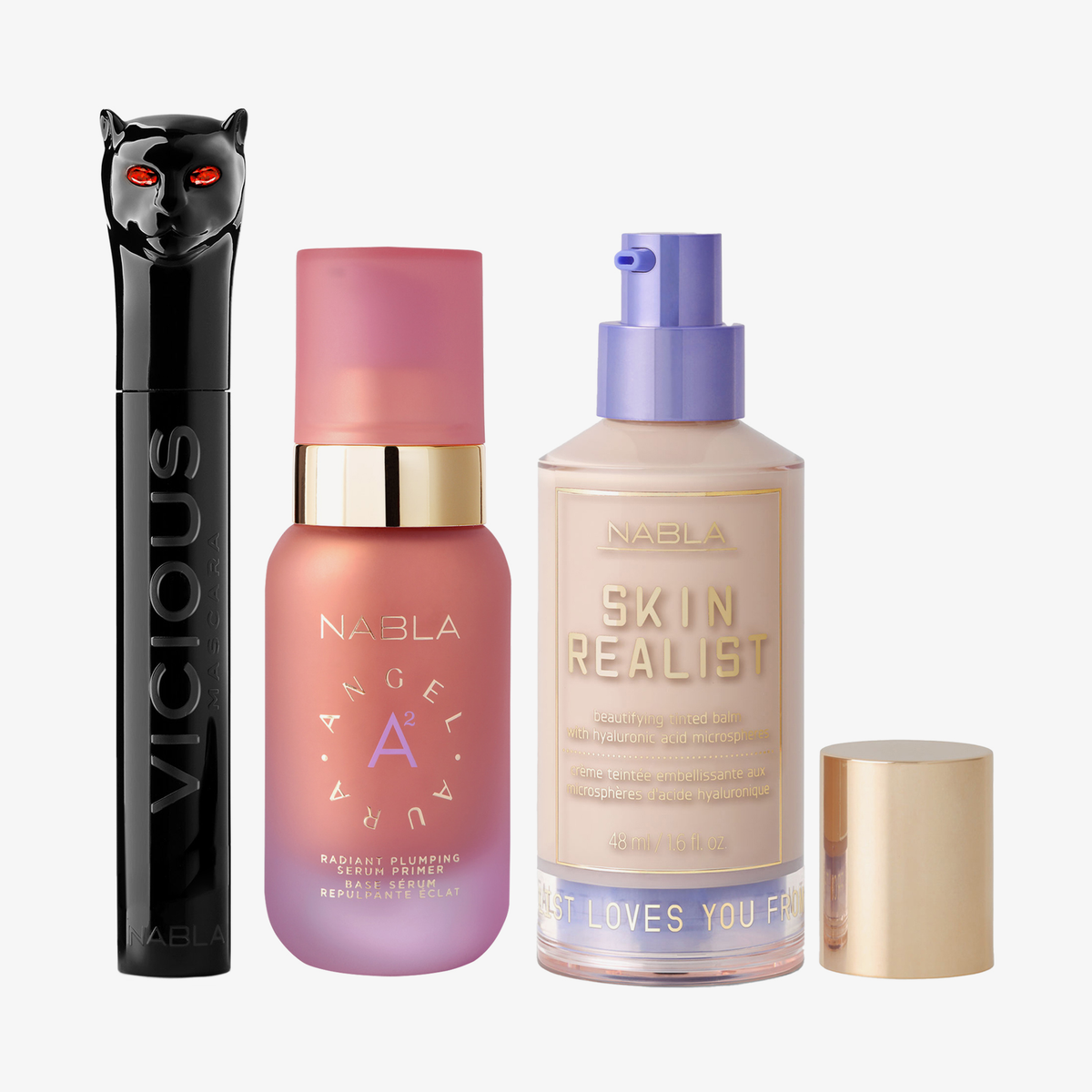 Drei NABLA-Produkte: schwarze Mascara mit Katzenkopf, rosa Angel Aura Serum-Primer und Skin Realist Tinted Balm in der Farbe 0.5 Fair mit lilafarbenem Pumpspender.