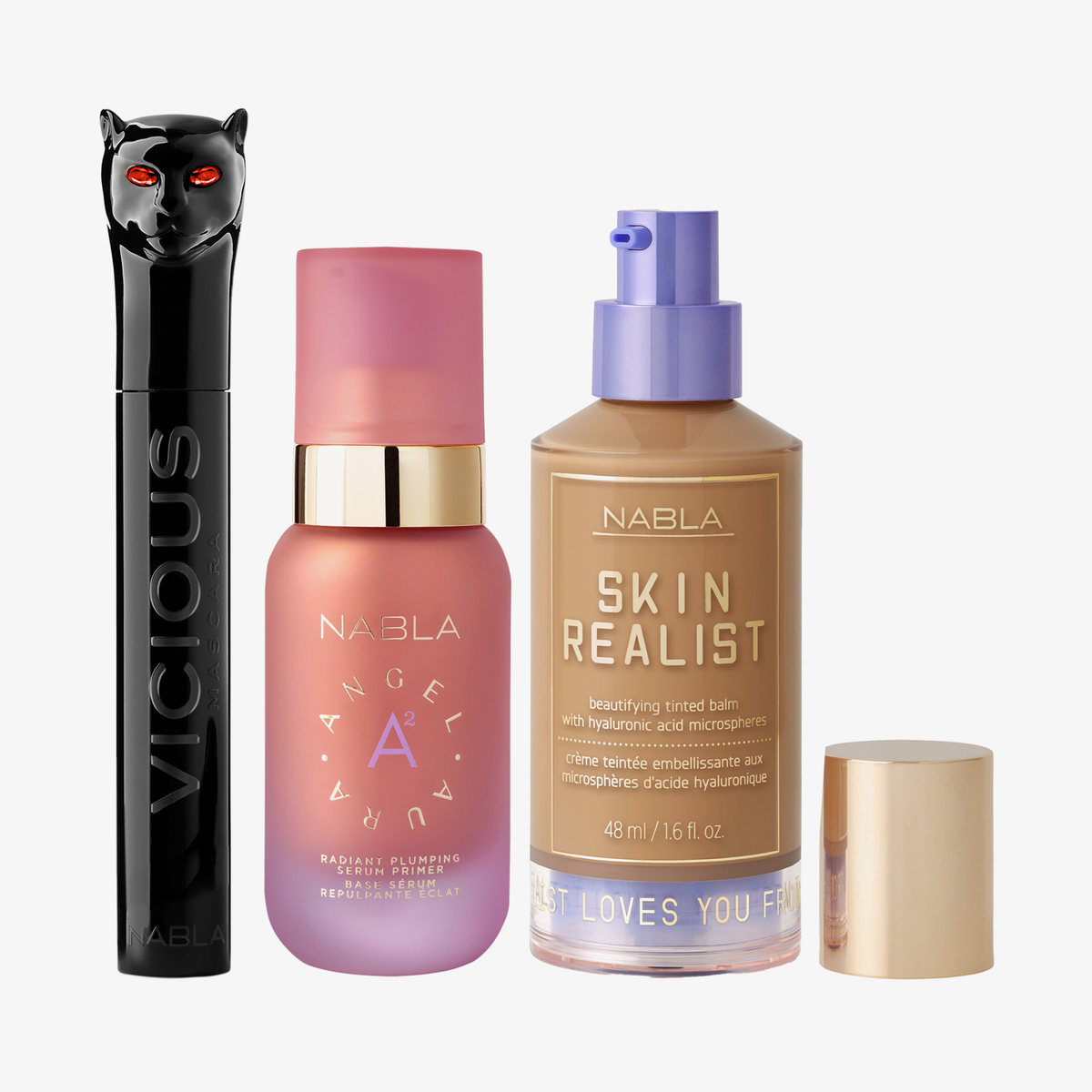 Drei NABLA-Produkte: schwarze Mascara mit Katzenkopf, rosa Angel Aura Serum-Primer und Skin Realist Tinted Balm in der Farbe 3.5 Medium-Tan mit lilafarbenem Pumpspender.