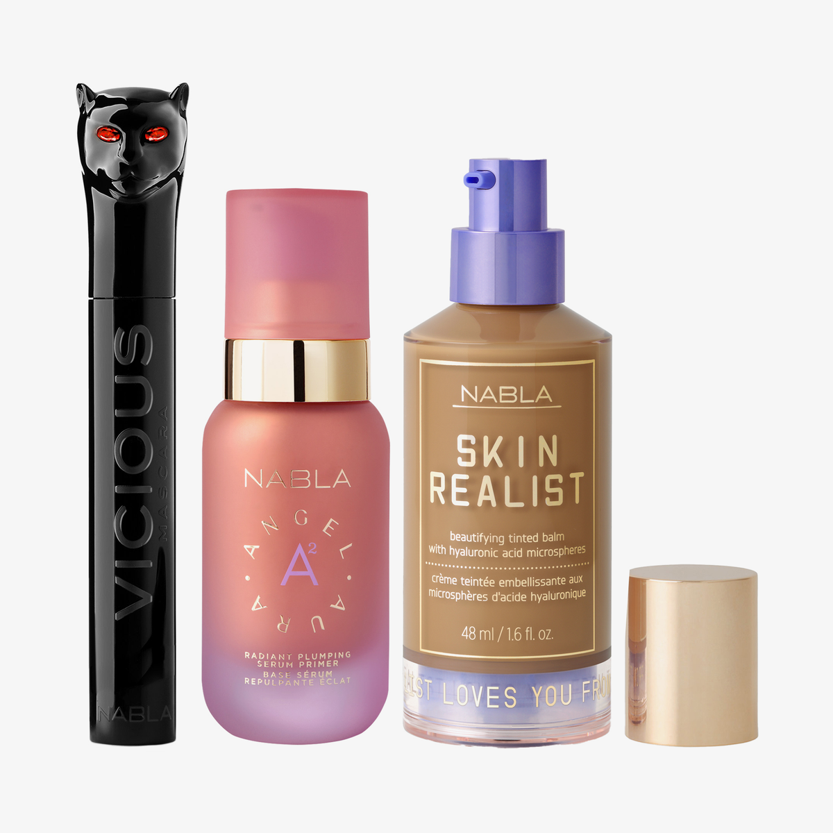 Drei NABLA-Produkte: schwarze Mascara mit Katzenkopf, rosa Angel Aura Serum-Primer und Skin Realist Tinted Balm in der Farbe 5 Tan mit lilafarbenem Pumpspender.