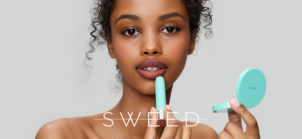 Eine Frau trägt Lippenstift auf, während sie einen Handspiegel hält; über dem Bild ist der Schriftzug „SWEED“ zu sehen, vor einem hellgrauen Hintergrund.
