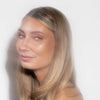 Eine Frau mit langem blondem Haar und strahlender Haut präsentiert glitzernden pfirsichdfarbenen Sparkl Flirt on LH Cosmetics.